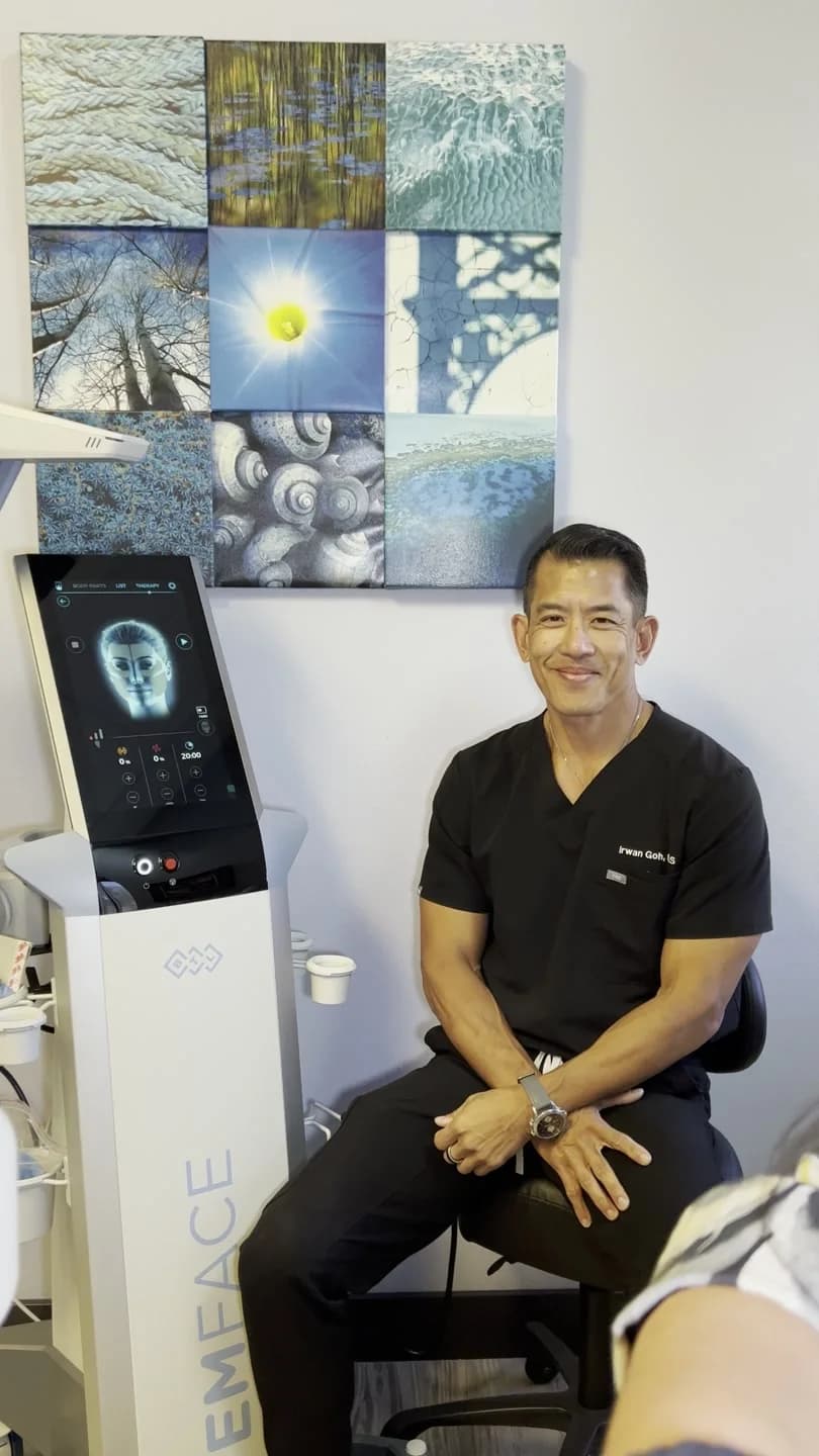 Dr. Irwan Goh, DDS, seated beside the EMFACE device in his Henderson practice