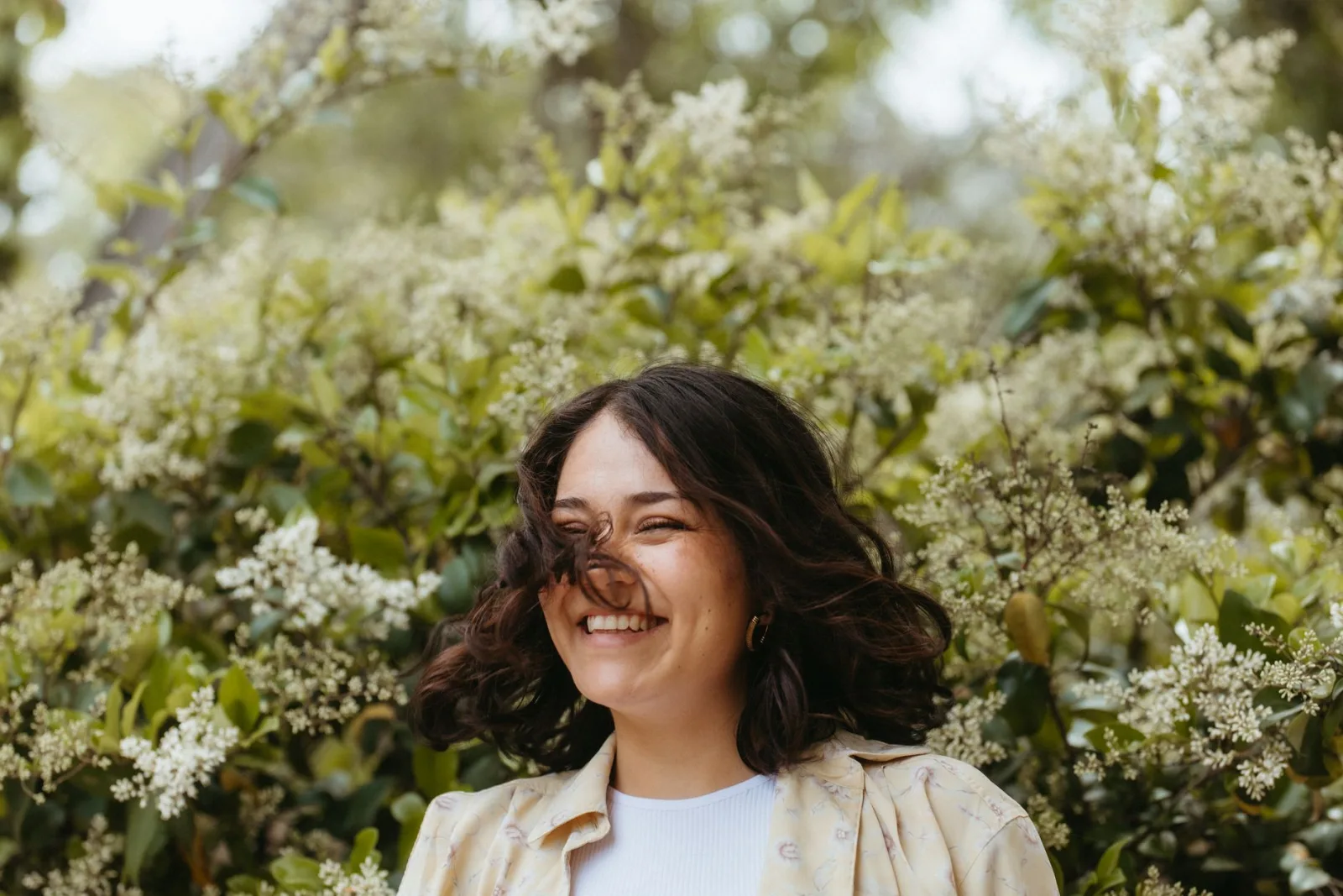 A woman laughing outdoors among flowering greenery in natural light