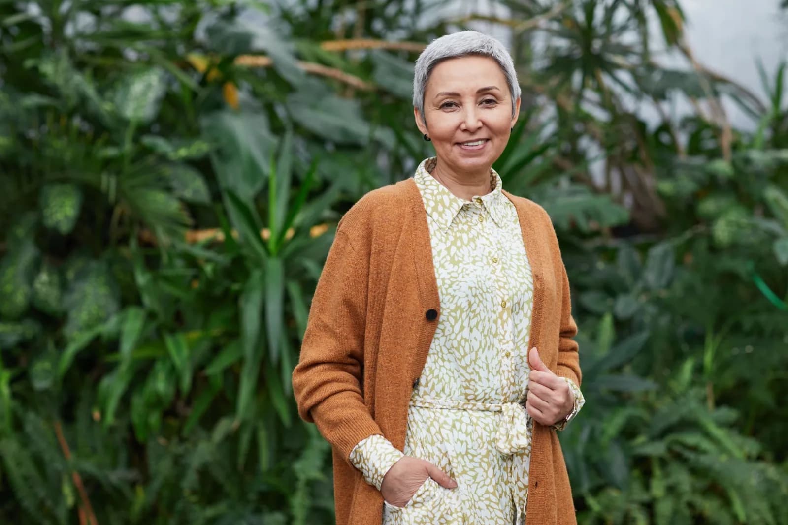 A woman in her sixties standing among greenery, relaxed and well